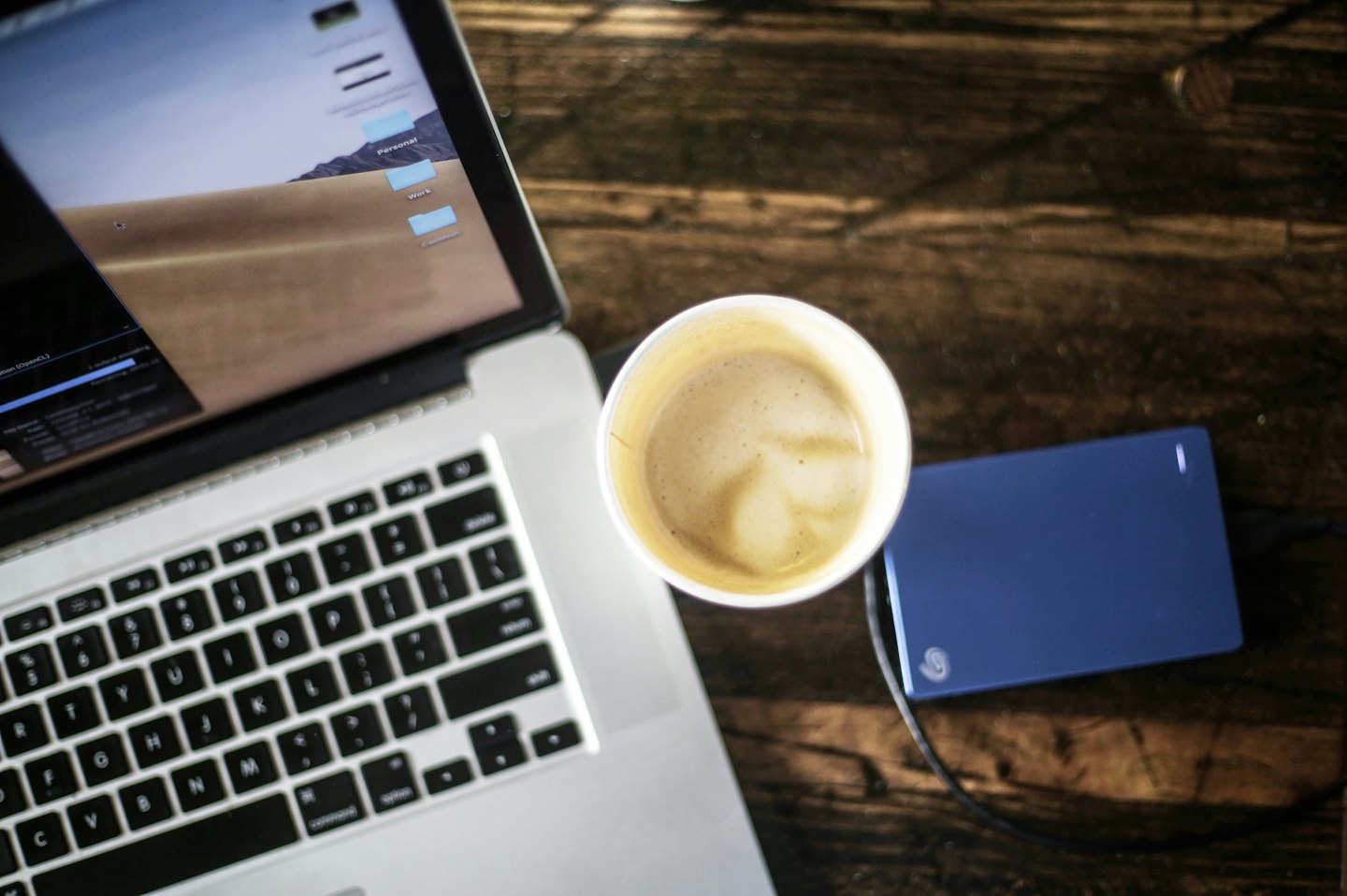 Laptop dengan folder kerja dan latte art di atas meja.