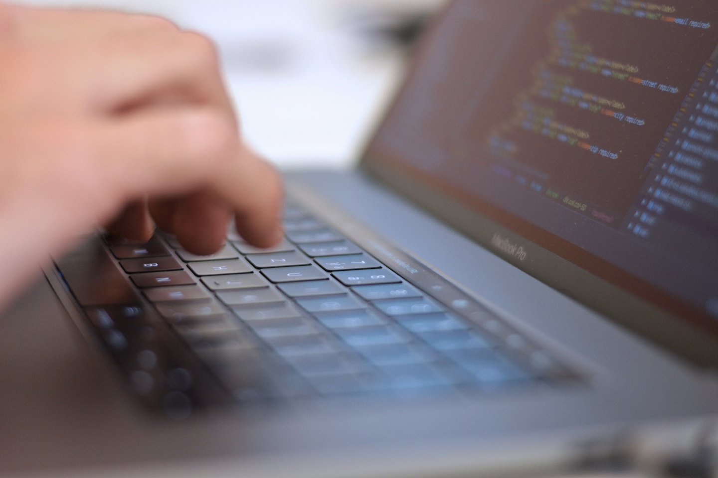 Tangan mengetik baris kode pemrograman di keyboard laptop.